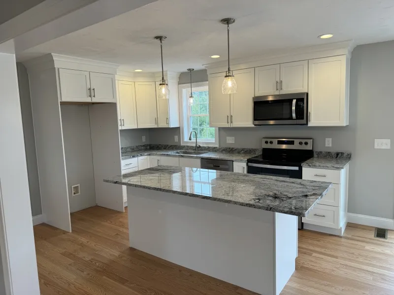 Modern kitchen with white cabinets, stainless appliances, and a marble island countertop.