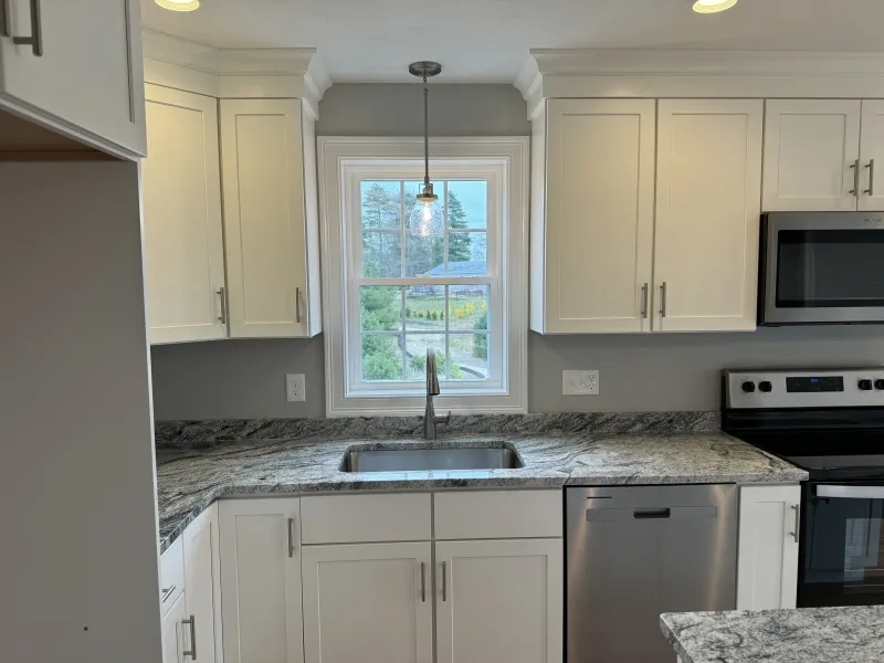 Modern kitchen with white cabinets, marble counters, and a window above the sink.
