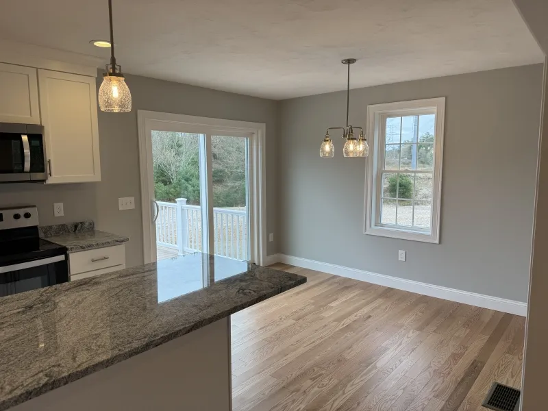 Modern kitchen and dining area with wood floors, pendant lights, and sliding glass door.