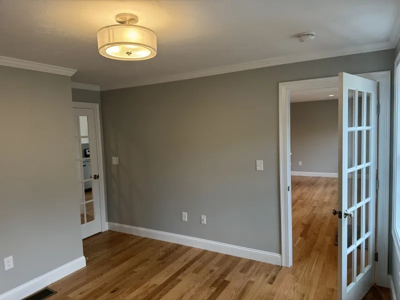 Empty room with light gray walls, wood floor, and glass-paned door open to another room.