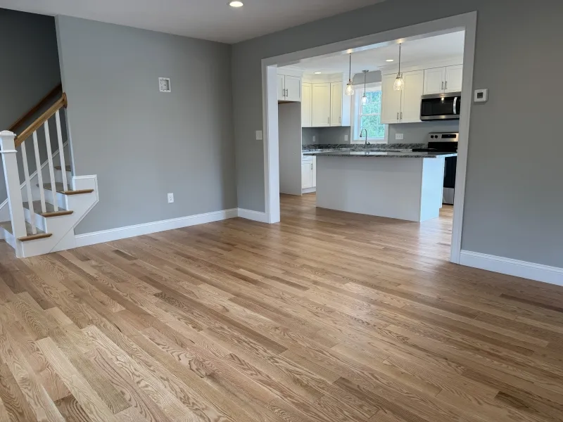 Spacious living area with hardwood floors, gray walls, and view into a modern kitchen.