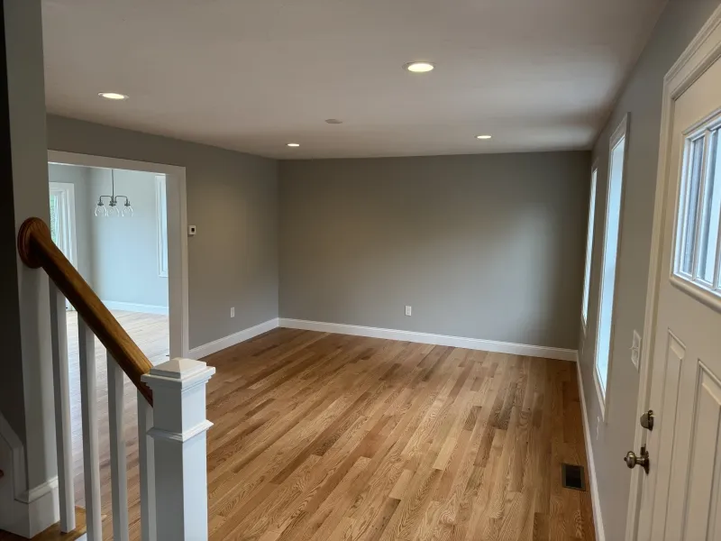 Empty living room with hardwood floors, gray walls, and recessed lighting by windows.
