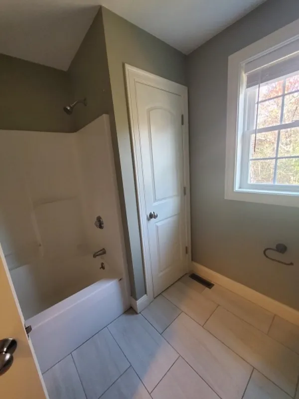 Bathroom with a bathtub, a closed door, a window, and a toilet paper holder on the wall.