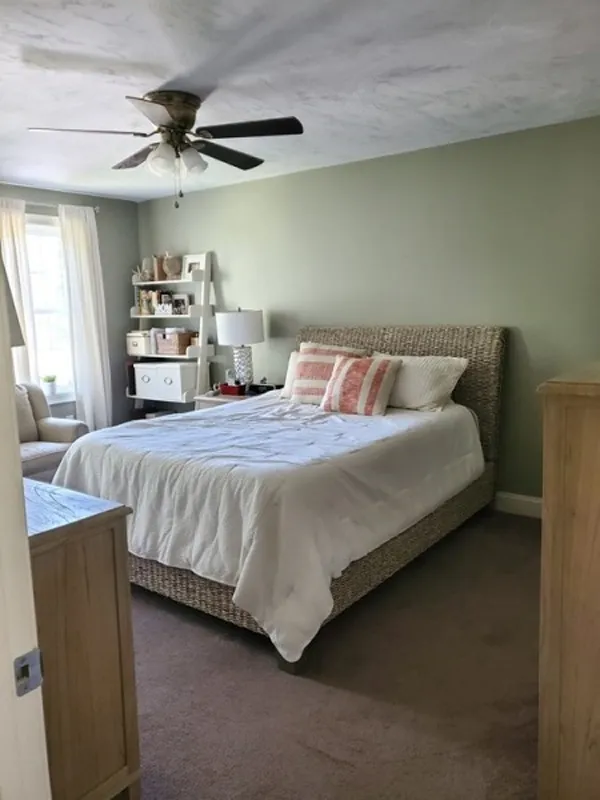 Bedroom with a wicker bed frame, white bedding, and a shelf by the window.