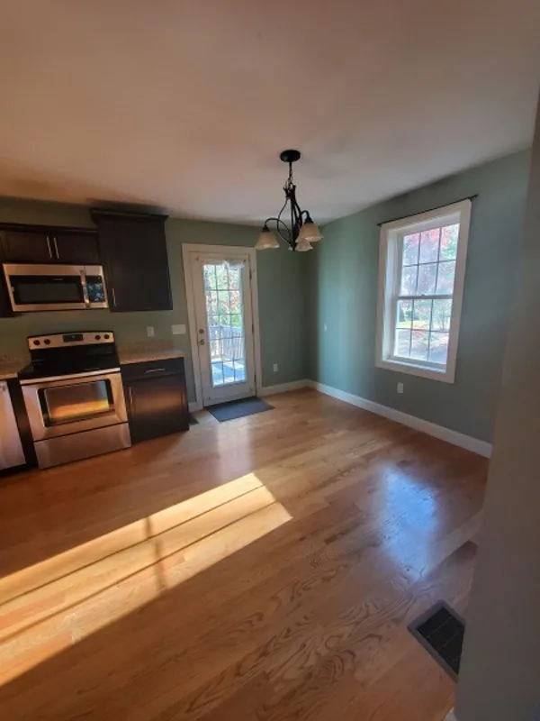 Kitchen with stainless appliances, wood floor, a window, and door to outside in sunlight.