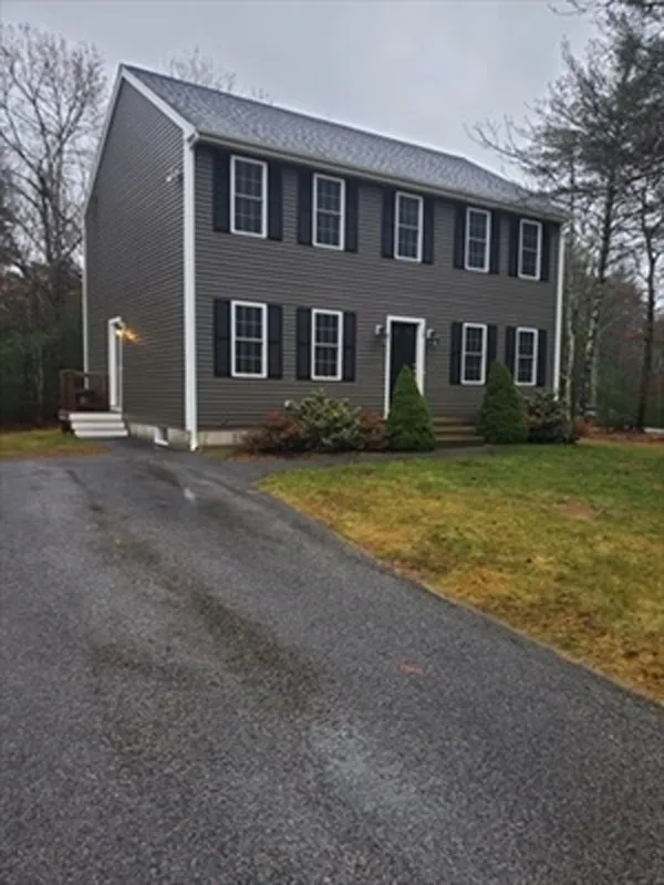Two-story gray house with black shutters, white trim, and a driveway on a cloudy day.