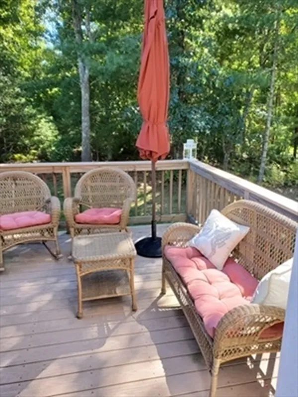 Wicker patio furniture with pink cushions and an orange umbrella on a wooden deck.
