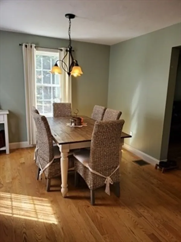 Dining table with six wicker chairs in a sunlit room with hardwood floors and green walls.