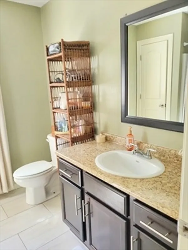 Bathroom with a granite countertop sink, wooden shelf, toilet, and mirror on the wall.