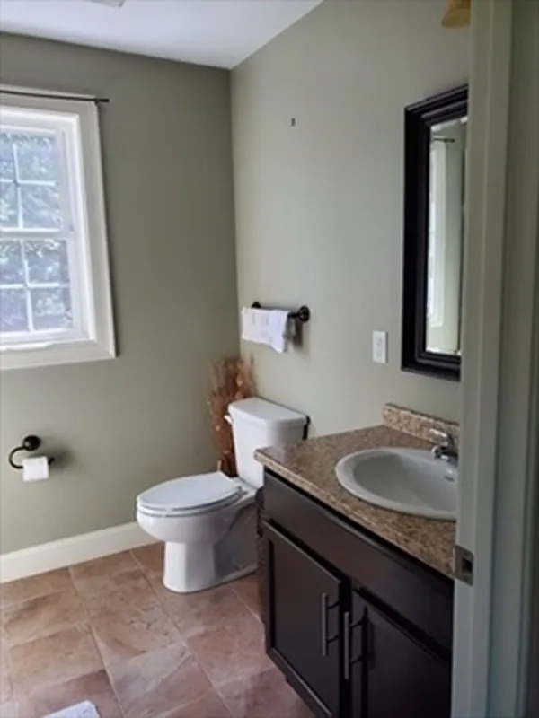 Bathroom with a toilet, sink, mirror, towel rack, and window with natural light.