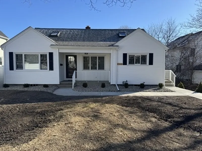 Single-story white house with black shutters, front porch, and bare yard under clear sky.