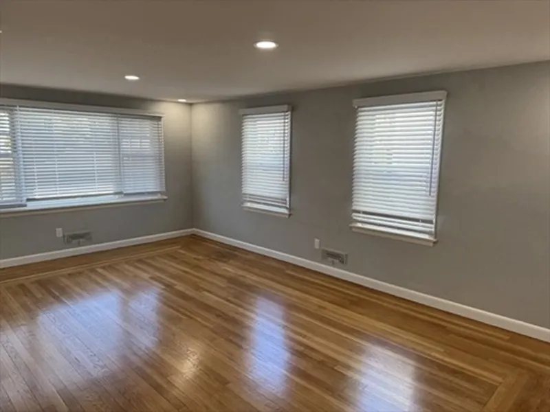 Empty room with hardwood floors, gray walls, three windows, and ceiling lights.