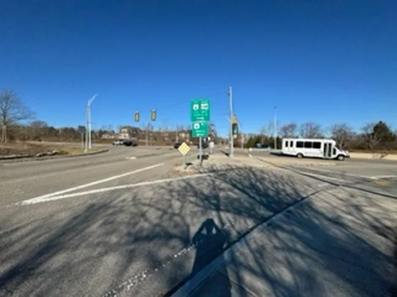 Intersection with green road signs, a white shuttle bus, and clear blue sky.