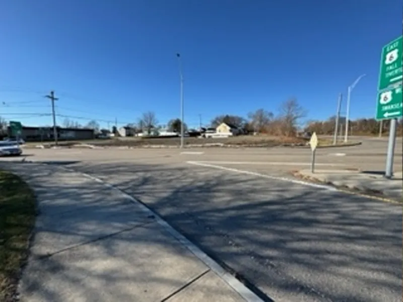 Sunny day at an empty intersection with road signs and a few buildings in the background.