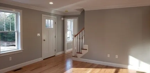 Empty room with light wood floors, gray walls, a window, door, and staircase.