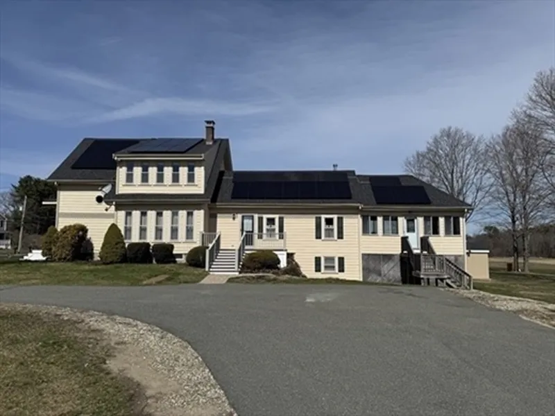 Yellow house with multiple solar panels on the roof, set beside a curved driveway.