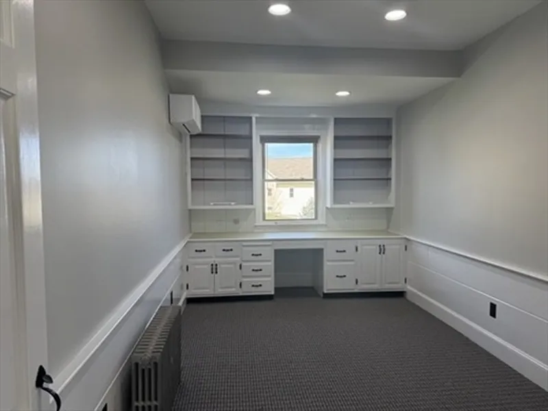 Home office with built-in white shelves, cabinets, a window, and recessed ceiling lights.