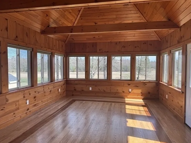 Sunroom with wood paneling, large windows, and hardwood floors, flooded with sunlight.