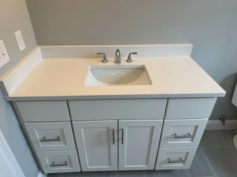White bathroom vanity with sink, chrome faucet, and six drawers against a gray wall.