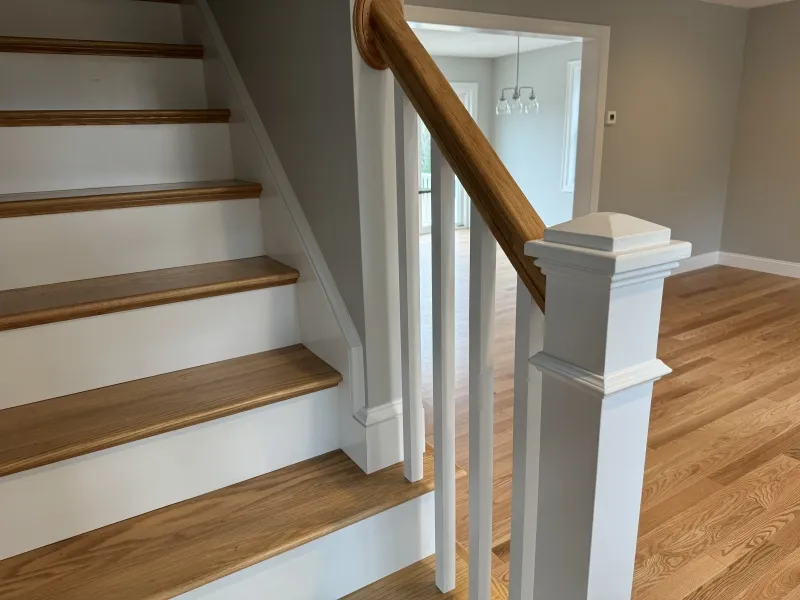 Wooden staircase with white risers and a handrail beside a light-finished wood floor.