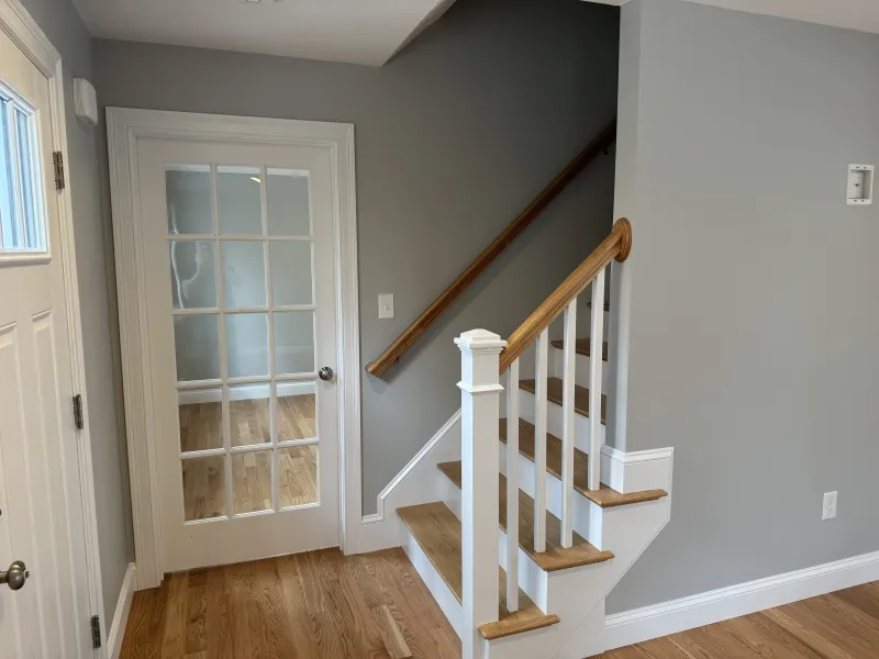 Small staircase with wooden steps beside a glass-panel door in a gray-walled entryway.