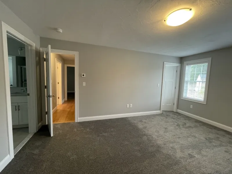 Empty bedroom with gray carpet, light gray walls, and a window with white trim.