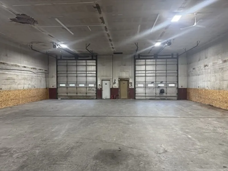 Empty industrial warehouse with two large garage doors and a concrete floor.