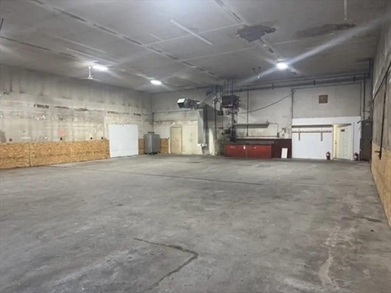 Large empty industrial warehouse with concrete floor, high ceiling, and some wall fixtures.