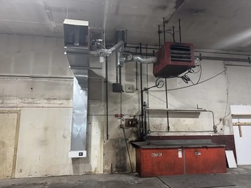 Red metal bins under industrial HVAC ducts and a heater mounted on a stained white wall.