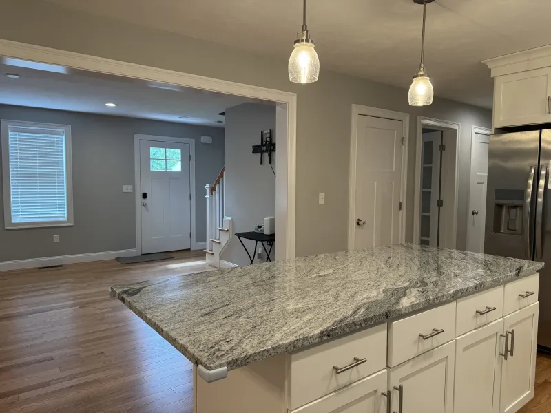 Modern kitchen with a marble island, white cabinets, and view of a bright entryway.