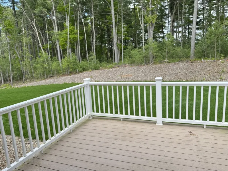 View from a wooden deck with white railing, facing a grassy yard and trees in the background.