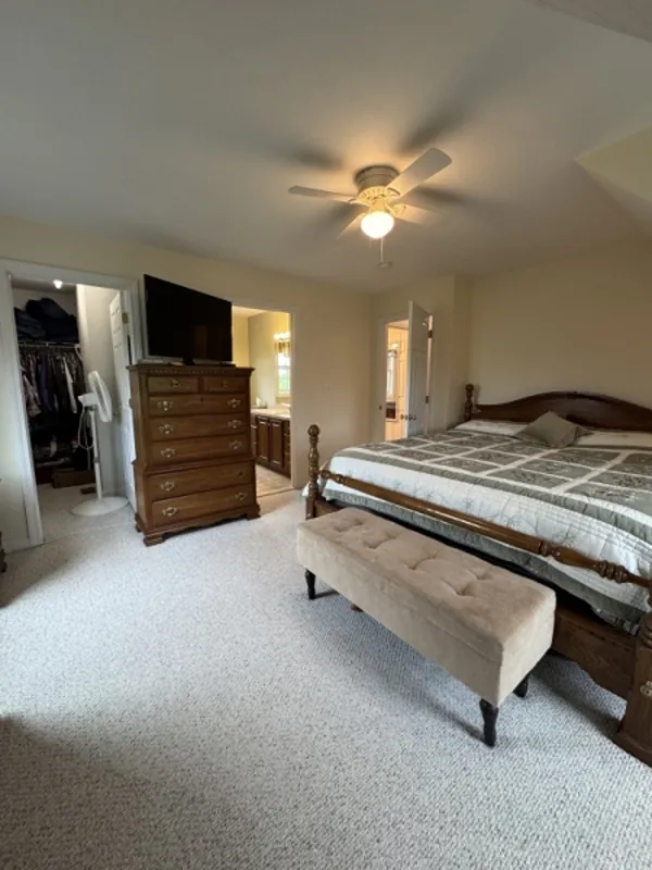 Bedroom with a bed, dresser, TV, ceiling fan, closet, and bench at the foot of the bed.