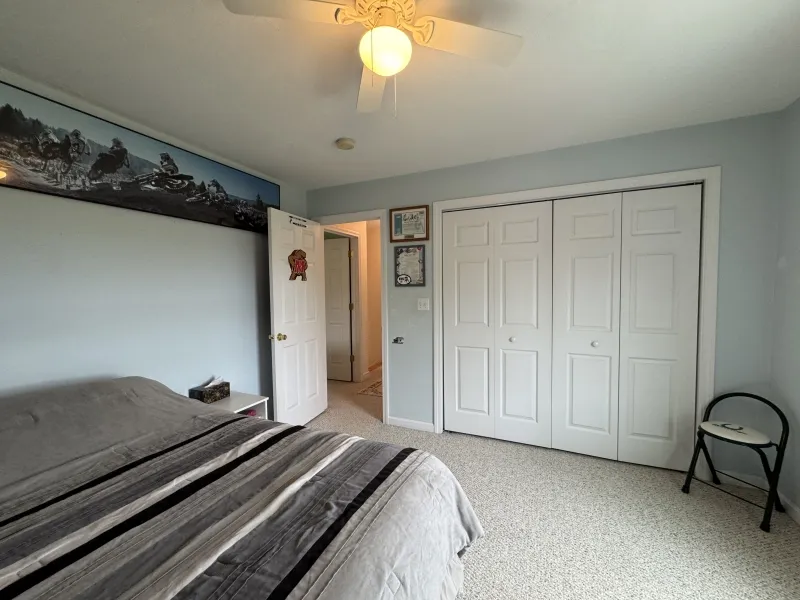 Bedroom with a striped bedspread, white closets, framed art, and a black folding chair.
