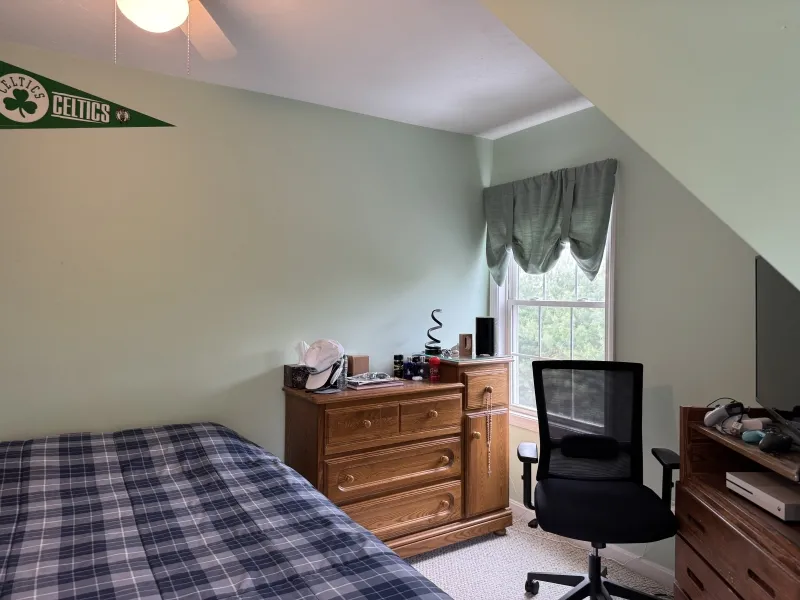 A bedroom with a bed, dresser, desk, chair, window, and a Celtics pennant on the wall.