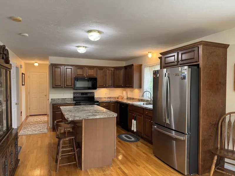 Modern kitchen with wood cabinets, granite island, stainless fridge, and hardwood floors.