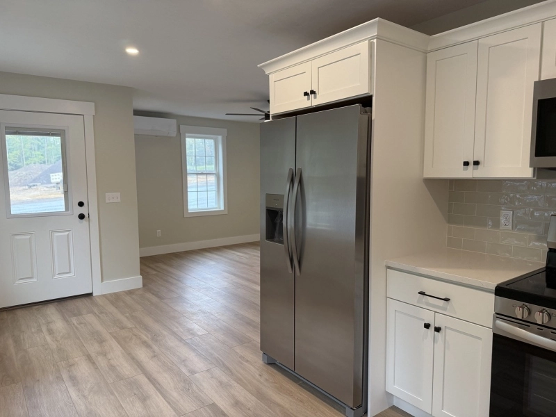 Modern kitchen with stainless steel fridge, white cabinets, and wood floors.