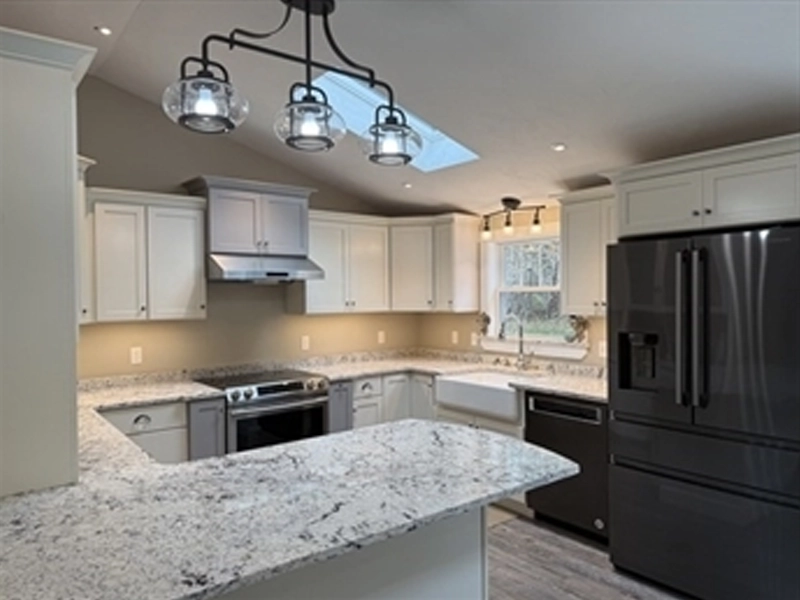 Modern kitchen with white cabinets, granite counters, black fridge, and pendant lighting.