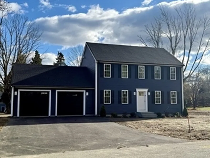 A two-story blue house with white trim and a double garage, under a partly cloudy sky.