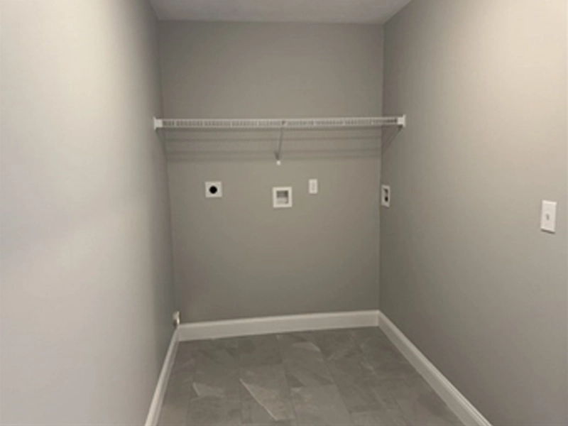 Empty laundry room with gray walls, tile floor, and a white wire shelf on the back wall.