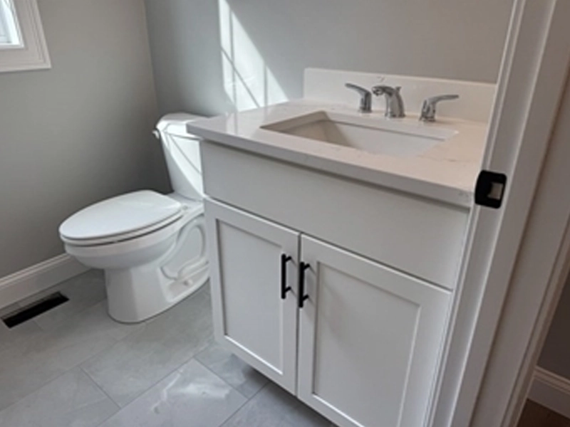 White bathroom with a toilet, white vanity, gray walls, and tiled floor.