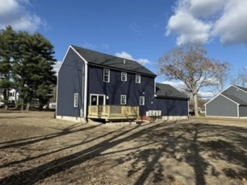 A navy blue house with a small wooden deck, set on a spacious yard under a blue sky.