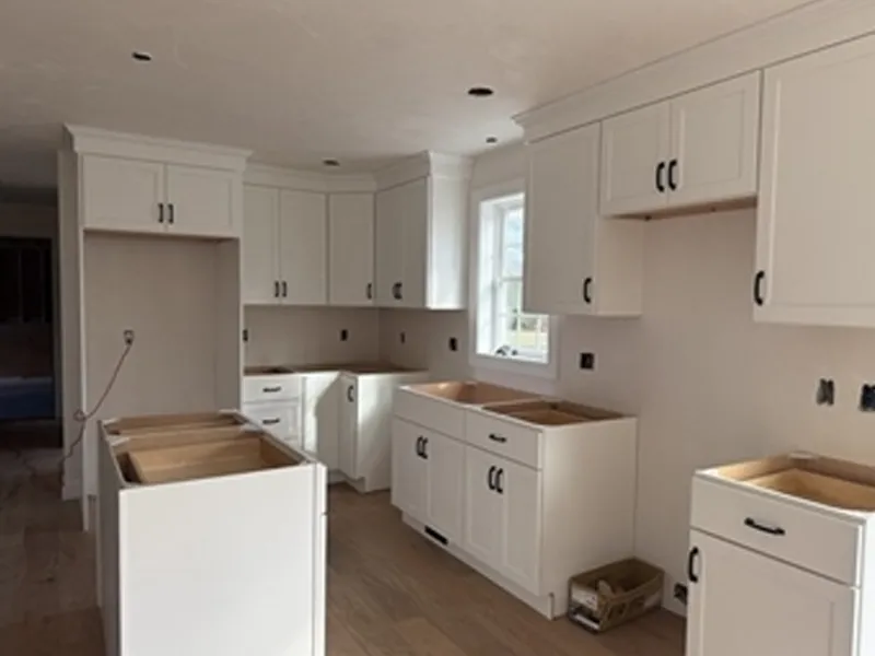 White kitchen cabinets being installed in a bright, unfinished kitchen space.