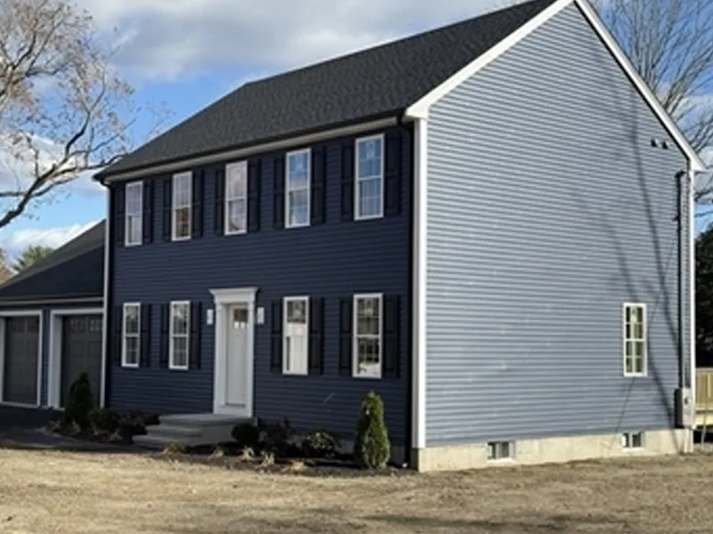 A two-story blue house with white trim and black shutters under a partly cloudy sky.