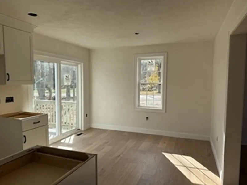 Empty room with light wood floors, white walls, and a large window and sliding glass door.