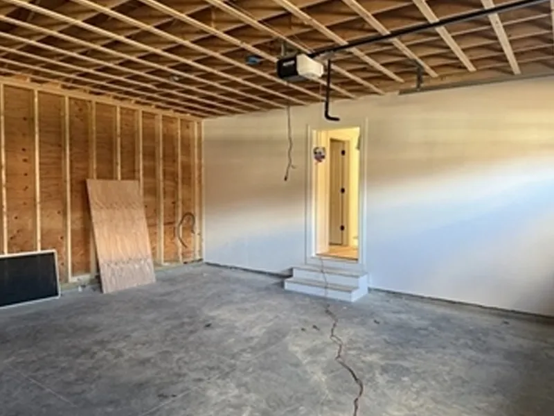 Unfinished garage with exposed wood framing, concrete floor, and a door with small steps.