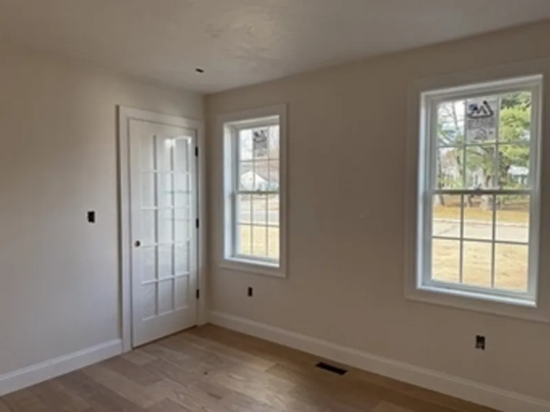 Empty room with light wood floor, two windows, and a white door with glass panels.