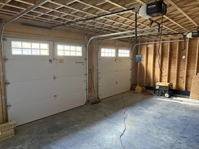 Unfinished garage with two white doors, exposed wooden beams, and a generator in the corner.