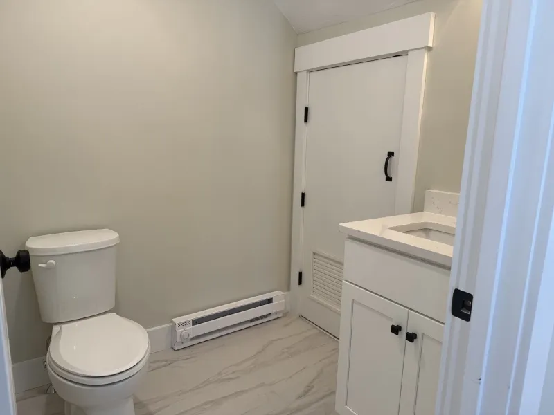 Small bathroom with a toilet, white vanity sink, and a door with a black handle.