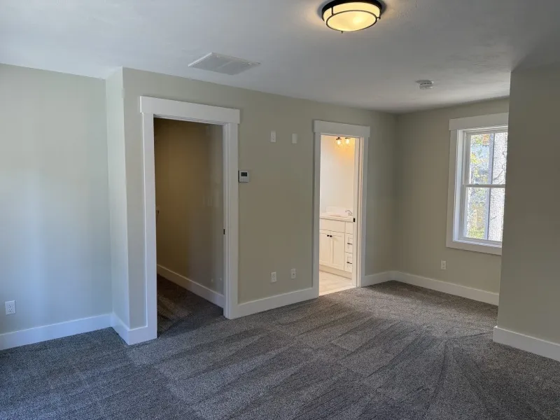Spacious, carpeted room with two doorways and a window letting in natural light.