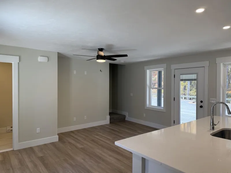 Modern living area with wood floors, ceiling fan, and kitchen island near patio doors.